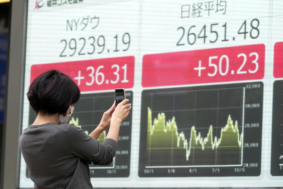 A person takes photos of an electronic stock board showing Japan's Nikkei and New York Dow indexes at a securities firm Wednesday, Oct. 12, 2022, in Tokyo. Asian shares were mostly lower on Wednesday following another volatile day on Wall Street, as traders braced for updates on inflation and corporate earnings. (AP Photo/Eugene Hoshiko)