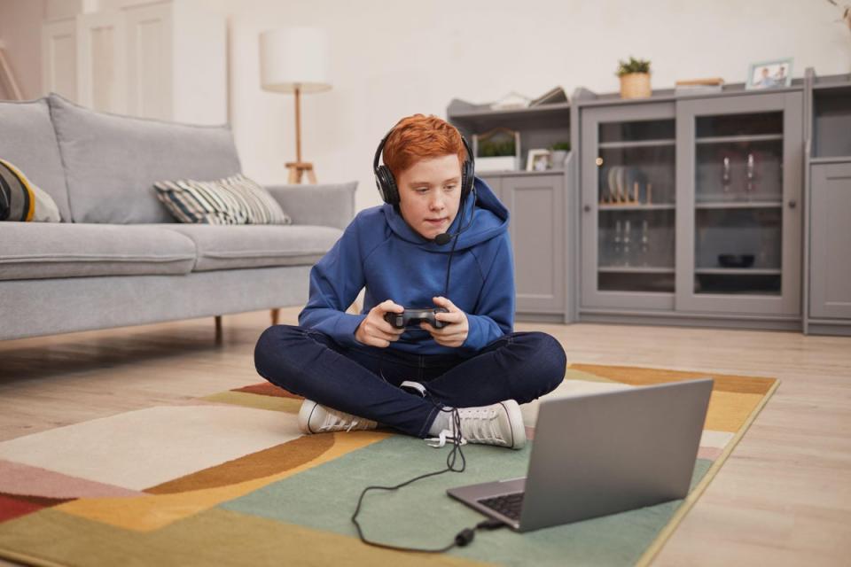 2E4N1HR Full length portrait of red haired teenage boy playing video games while sitting on floor and holding gamepad, copy space