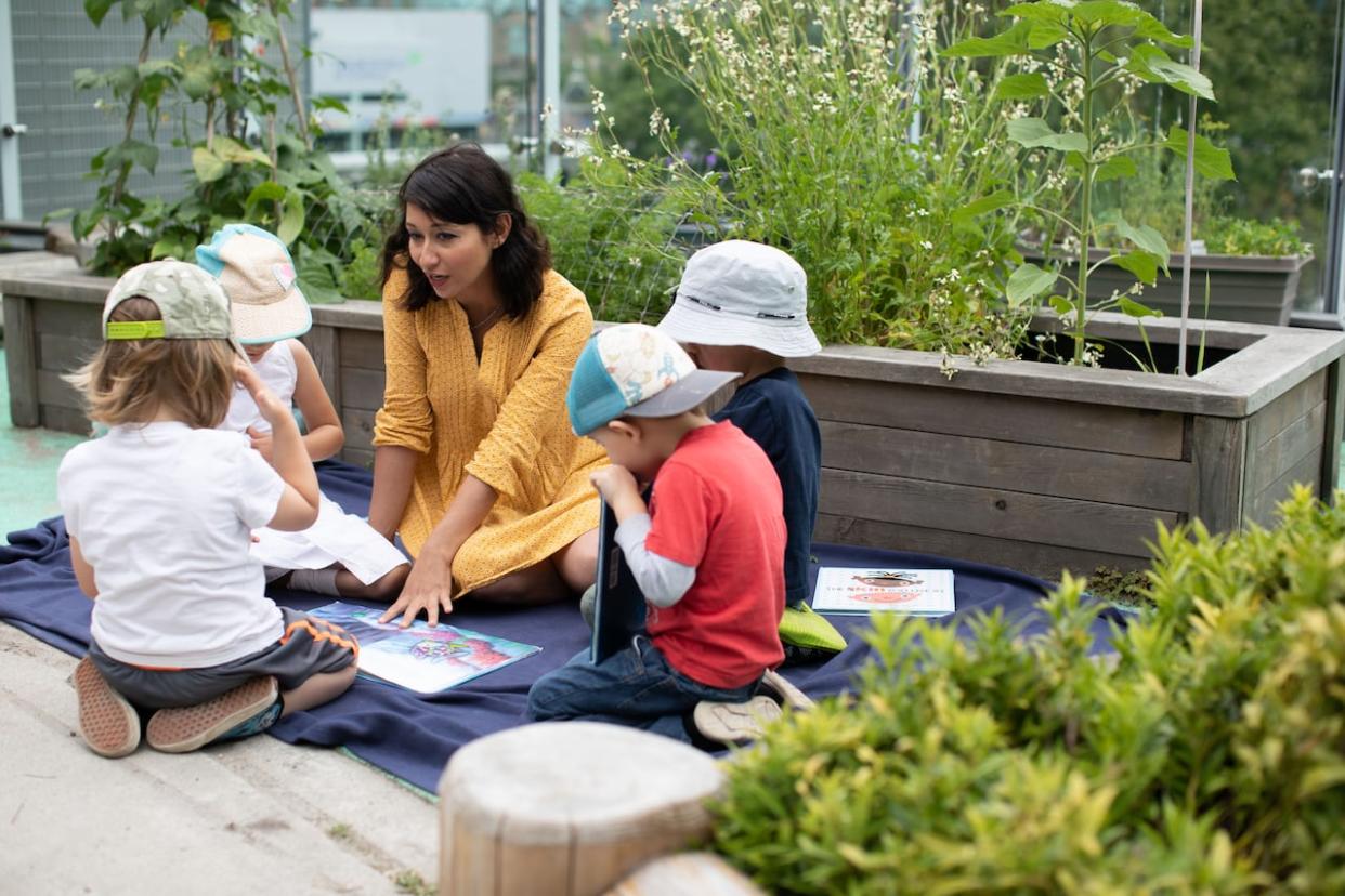 A child-care worker in Vancouver reads to children in this file photo from 2019, when the provincial government announced a partnership with the City of Vancouver that would bring thousands of new licensed child-care spaces to parents across the city. (Maggie MacPherson/CBC - image credit)