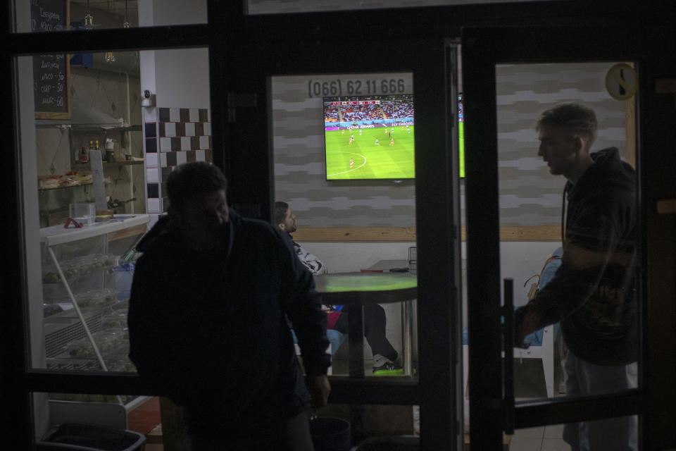 People watch a World Cup soccer match on a screen, in Mazza Cafe kebab-stand in Irpin, Kyiv region, Ukraine, Tuesday, Nov. 29, 2022. For soccer lovers in Ukraine, Russia's invasion and the devastation it has wrought have created uncertainties about both playing the sport and watching it. For Ukrainians these days, soccer trails well behind mere survival in the order of priorities. (AP Photo/Andrew Kravchenko)