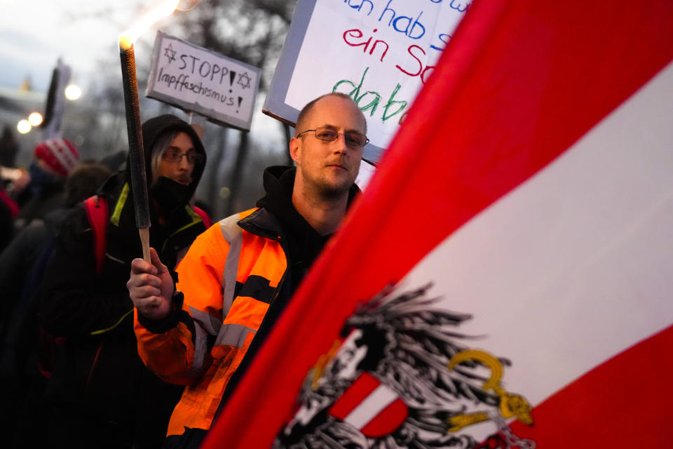A protestor holds a flare as he walks behind an Austrian national flag during a demonstration against measures to battle the coronavirus pandemic in Vienna, Austria, Saturday, Nov. 20, 2021. Thousands of protesters are expected to gather in Vienna after the Austrian government announced a nationwide lockdown to contain the quickly rising coronavirus infections in the country. Poster in background reads: 'Stop the vaccination fascism'.(AP Photo/Florian Schroetter)