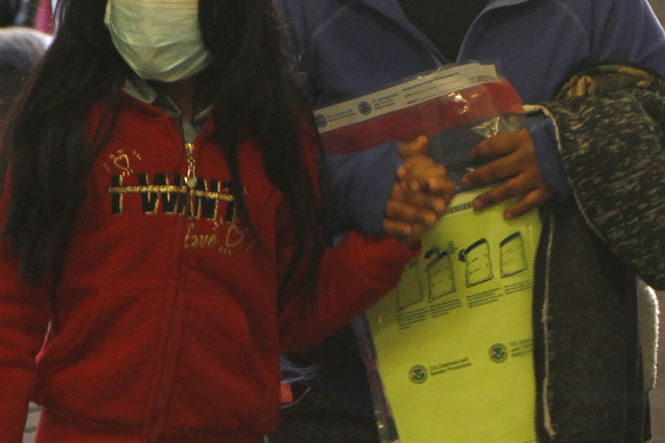 A woman carries a property bag issued by Customs and Border Protection while holding the hand of a girl wearing a mask as they arrive at a mandatory immigration court hearing on Monday, March 16, 2020, in El Paso, Texas. The migrants, who must wait in Ciudad Juarez, Mexico, wore masks following the first reported cases of COVID-19 in El Paso. The migrants are not suspected to be carrying the virus. (AP Photo/Cedar Attanasio)