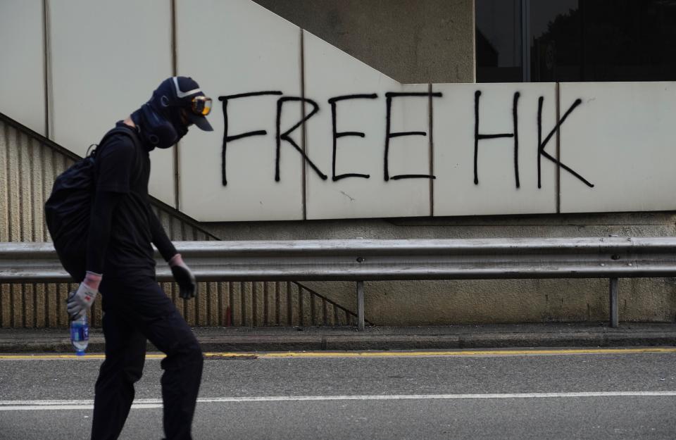 A protestor walks past a graffiti in Hong Kong, Sunday, Sept. 29, 2019. Riot police fired tear gas Sunday after a large crowd of protesters at a Hong Kong shopping district ignored warnings to disperse in a second straight day of clashes, sparking fears of more violence ahead of China's National Day. (AP Photo/Vincent Yu)