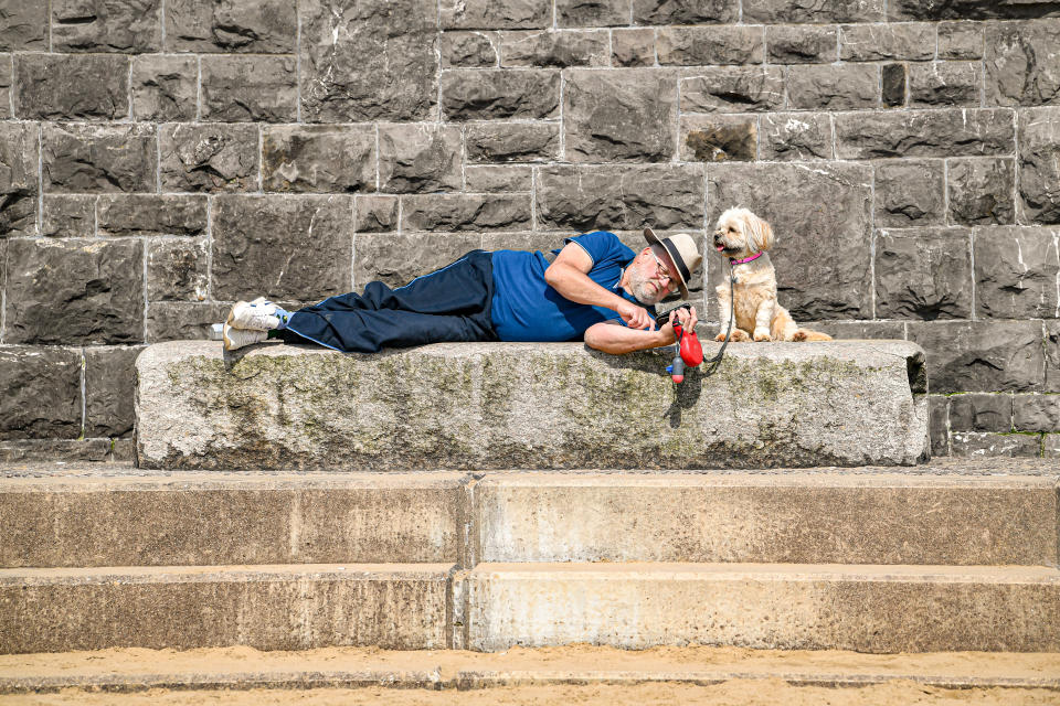 <p>A man relaxes with his dog on the beach at Weston-super-Mare, Somerset, in warm weather. Picture date: Tuesday April 20, 2021.</p>
