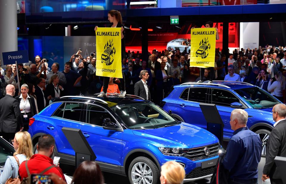 Greenpeace activists standing on Volkswagen (VW) cars hold posters reading "Climate Killers" as they demonstrate at the booth of Volkswagen, where German Chancellor Angela Merkel touring the fair grounds was expected after officially opening the International Auto Show (IAA) in Frankfurt am Main, western Germany, on September 12, 2019. - Climate protection protesters say the car sector is failing to reduce carbon emissions despite a massive push for new electric vehicles. (Photo by Tobias SCHWARZ / AFP)        (Photo credit should read TOBIAS SCHWARZ/AFP/Getty Images)