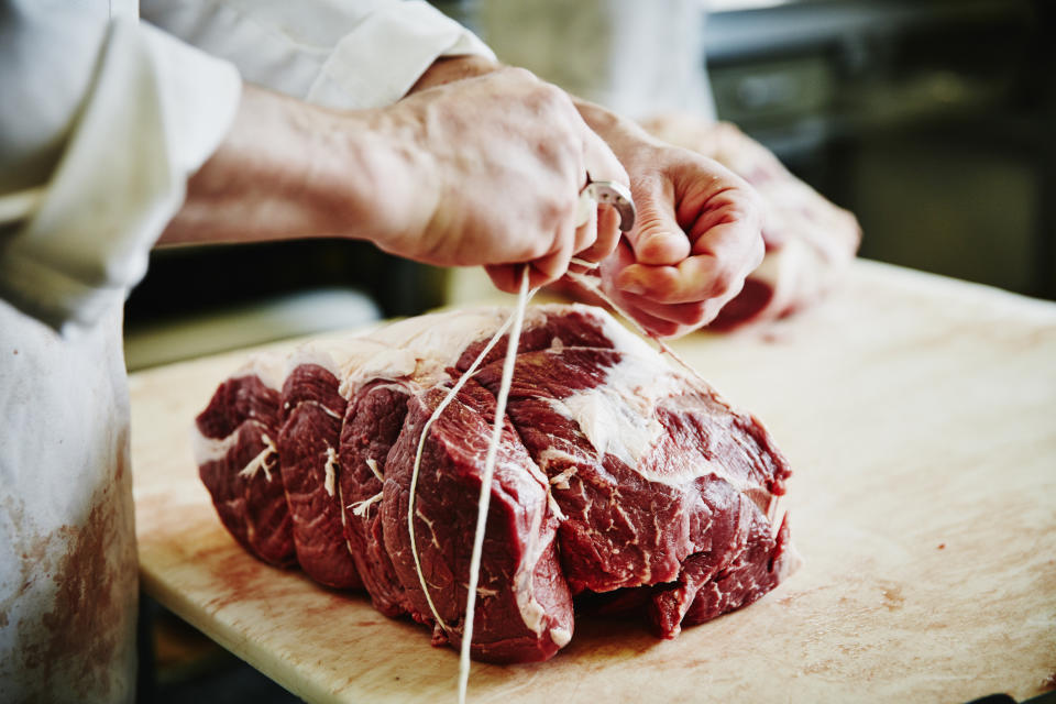 A butcher ties a piece of raw beef with twine on a wooden cutting board