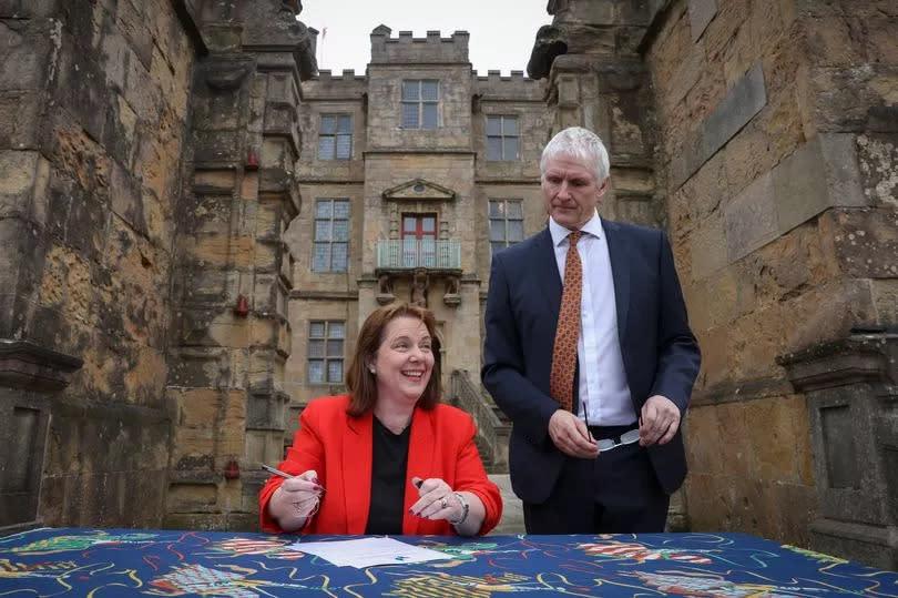 Claire Ward, the newly elected mayor of the East Midlands Combined County Authority signs the mayoral declaration alongside Mark Rogers, the interim chief executive of the East Midlands Combined County Authority at Bolsover Castle in Derbyshire. Clair is wearing a black top and red jacket, whilst Mark is wearing a dark suit, white shirt and orange tie.