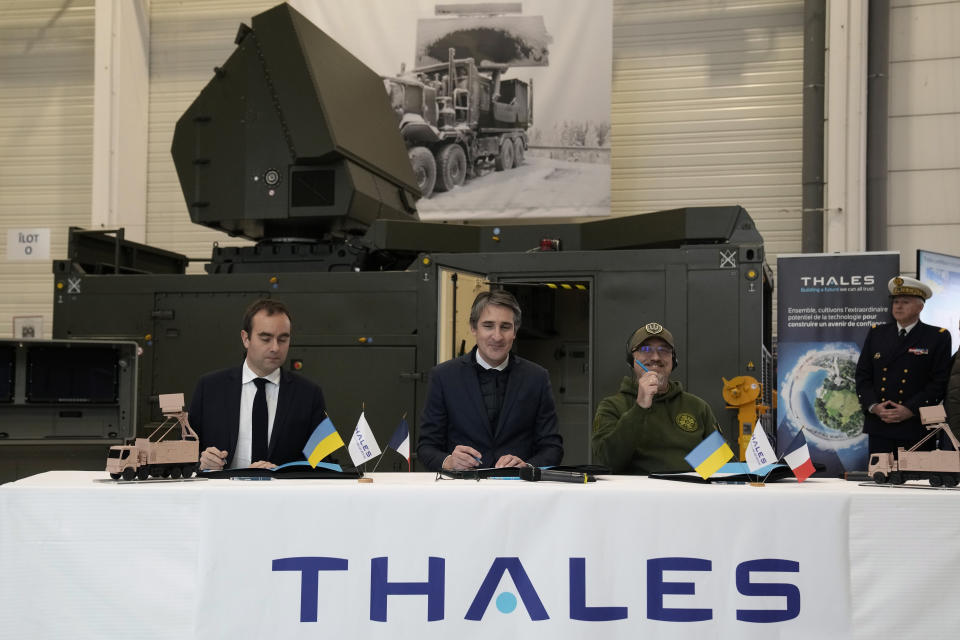 French Defense Minister Sebastien Lecornu, left, and Ukrainian Minister of Defense Oleksii Reznikov, right, sign an agreement with Chairman and CEO of Thales Group Patrice Caine, center, during a visit at Thales radar factory in Limours, south west of Paris, France, Wednesday, Feb. 1, 2023. France has guaranteed Kyiv the delivery of a Ground Master 200 (GM200) radar, produced by the French manufacturer Thales. This medium-range radar is capable of spotting enemy aircraft at 250 km and engaging them at 100 km, whether they are flying at low speed and low altitude like drones or at high altitude like fighter planes. (AP Photo/Christophe Ena)