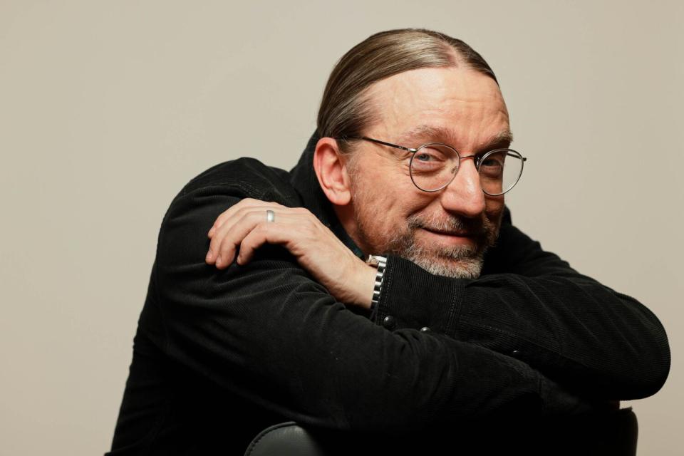 A man in a black sweater sits on a chair.