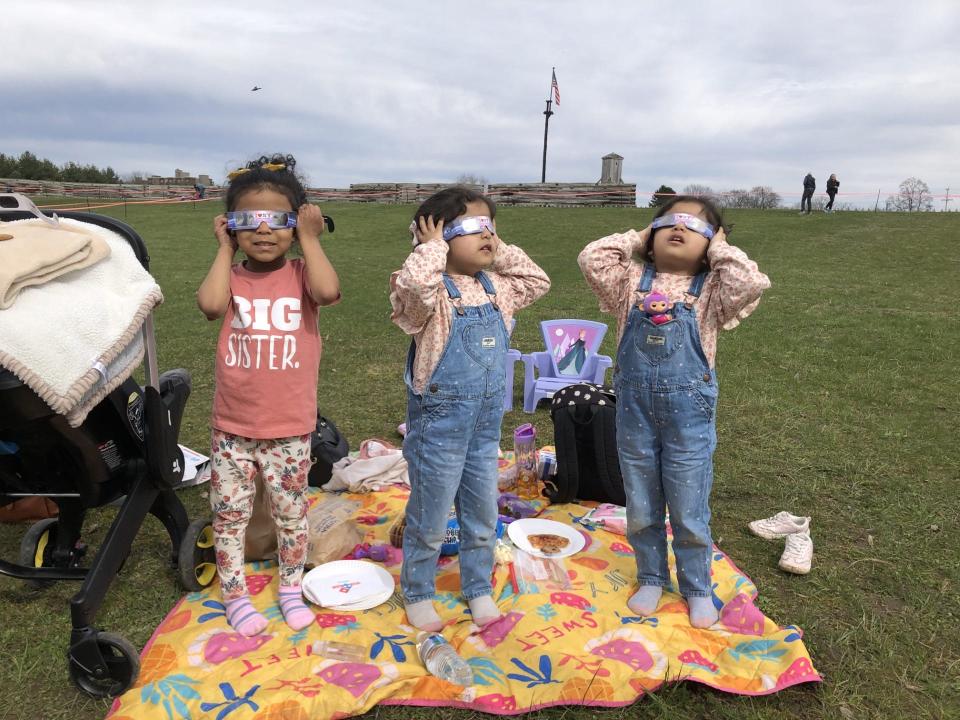 Marianna Wilson, 3, and twins Goudia, center, and Sofia, right, Dabraim, 4, all of Rome, model their eclipse glasses after the height of the eclipse on April 8, 2024 at Fort Stanwix National Monument in Rome.