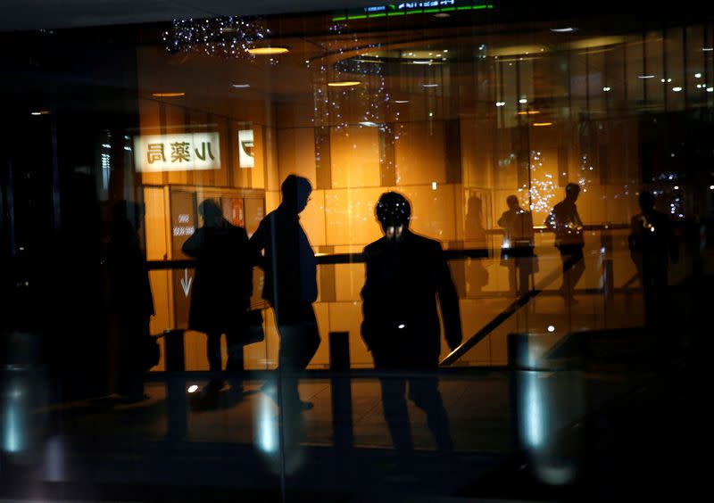 FILE PHOTO: Pedestrians are reflected on a window of a commercial building at closing hour at a financial district in Tokyo