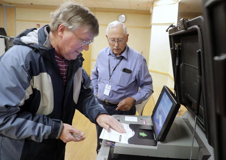 Poll worker Jerry Desens helps Lynn Wussow cast his ballot at the Grand Chute Town Hall.