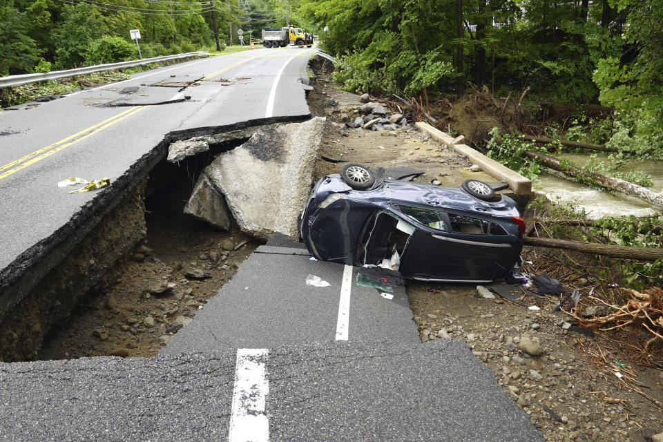 A car on its side on a collapsed roadway with debris all around.