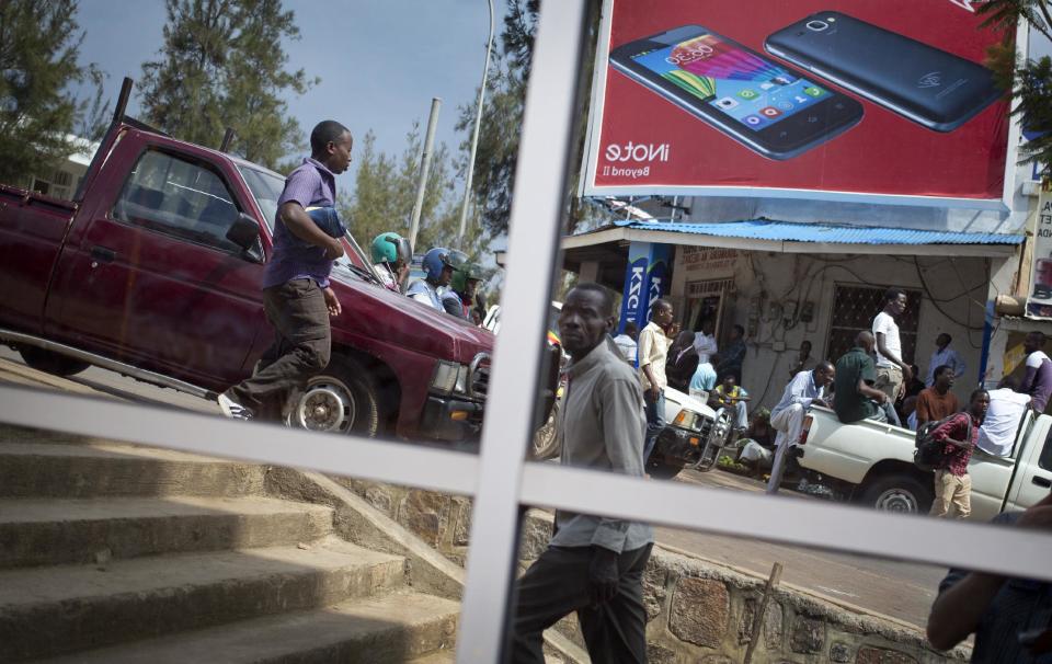 In this photo taken Tuesday, March 25, 2014, Rwandans seen reflected in the windows of an office building go about their daily business in downtown Kigali, Rwanda. Although Rwanda has made significant progress since the genocide, ethnic tensions remain. (AP Photo/Ben Curtis)