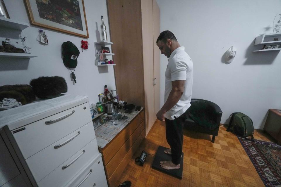 Iranian wrestler Iman Mahdavi, 28, checks his weight at his home in Milan, northern Italy, Thursday, Feb. 29, 2024. Mahdavi fled his home country in fear of his life in October 2020. Now, he will compete in Paris as part of the Refugee Olympic Team. (AP Photo/Luca Bruno)