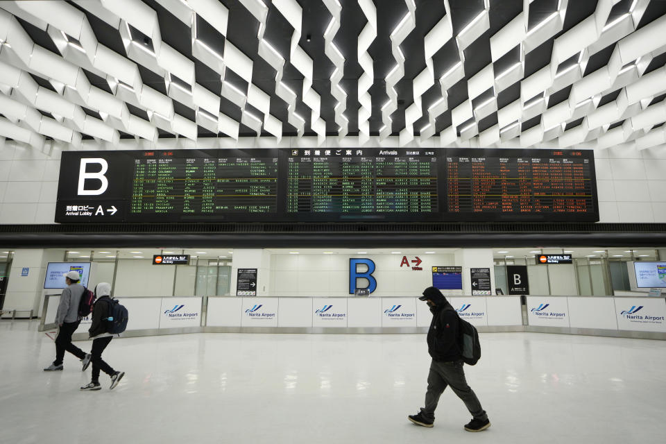 Passengers walk by arrival information screens for international flights at the Narita International Airport in Narita, east of Tokyo, Thursday, Dec. 2, 2021. Going further than many other countries in trying to contain the virus, Japan has banned foreign visitors and asked international airlines to stop taking new reservations for all flights arriving in the country until the end of December. (AP Photo/Hiro Komae)