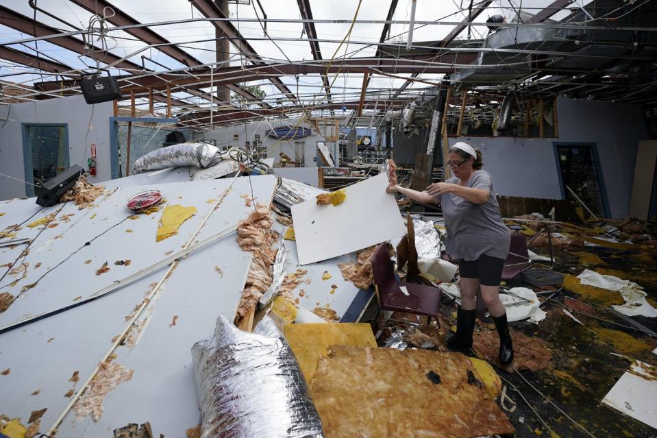 Woman sorts through soggy materials in roofless building