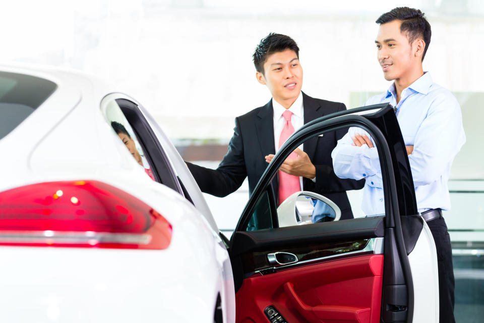 Two Asian men talk next to a car.