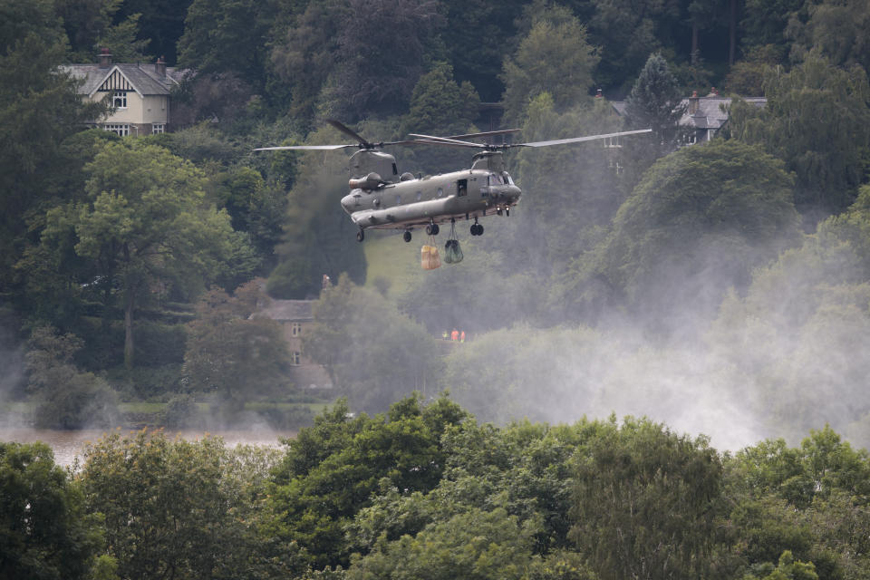An RAF Chinook helicopter drops aggregate to help shore up a reservoir at risk of collapse, threatening to engulf the town of Whaley Bridge in the Peak District, England, Friday, Aug. 2, 2019. A British military helicopter has dropped sandbags to shore up a reservoir wall as emergency services worked frantically to prevent a rain-damaged dam from collapsing. Engineers say they remain "very concerned" about the integrity of the 19th-century Toddbrook Reservoir, which contains around 1.3 million metric tons (1.5 million (U.S tons) of water. (AP Photo/Jon Super)