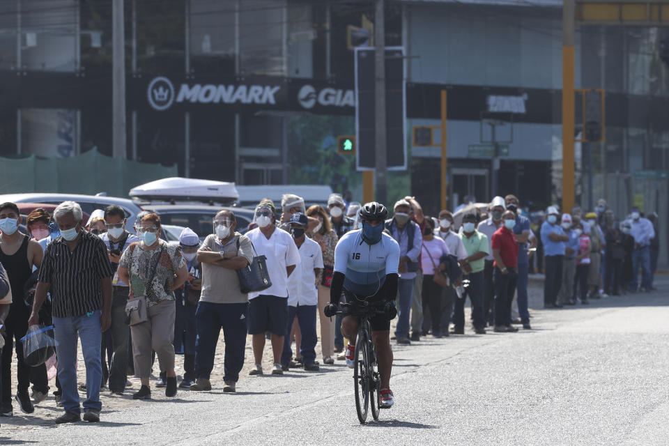 A cyclist pedals along voters wearing masks to curb the spread of the new coronavirus lining up to enter a polling station during general elections in Lima, Peru, Sunday, April 11, 2021. (AP Photo/Martin Mejia)