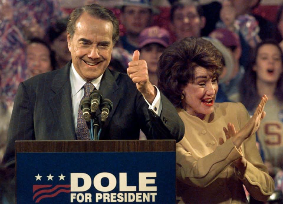 Bob and Elizabeth Dole interact with crowd members while standing behind a podium with a sign that says 