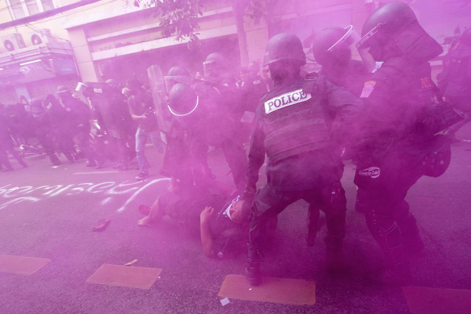 In cloud of pink smoke, police in riot gear remove a protester trying to march to the Asia-Pacific Economic Cooperation APEC summit venue, Friday, Nov. 18, 2022, in Bangkok, Thailand. (AP Photo/Wason Wanichakorn)