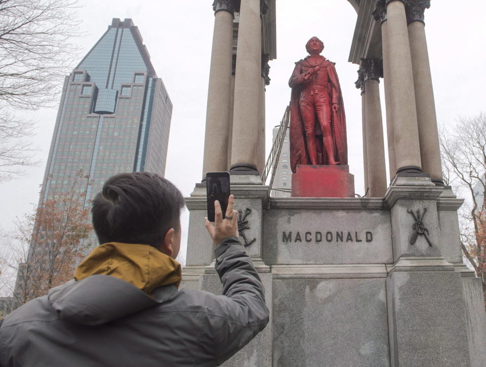 A man takes a photo of a statue of Sir John A. Macdonald after it was vandalized Monday, November 13, 2017 in Montreal. The statue appears covered in what appeared to be red paint with profanity painted at the base of the monument. (Photo by Ryan Remiorz, The Canadian Press)