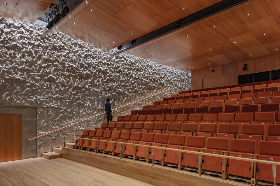 Crinkled concrete walls and cherry acoustical panels diffuse sound in the subterranean Justice Forum theater.