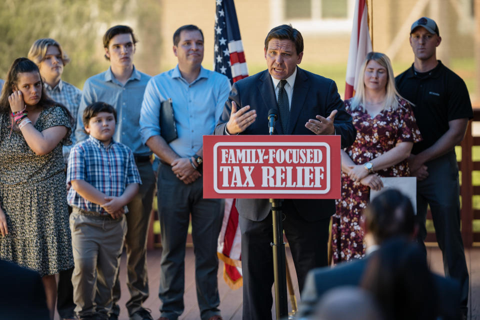 Gov. Ron DeSantis addresses a press conference at a podium marked: Family-Focused Tax Relief, surrounded by mostly young supporters. 