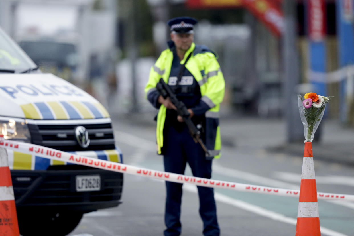 Flower rest at a road block, as a Police officer stands guard near the Linwood mosque, site of one of the mass shootings at two mosques in Christchurch, New Zealand, Saturday, March 16, 2019. (AP Photo/Mark Baker)