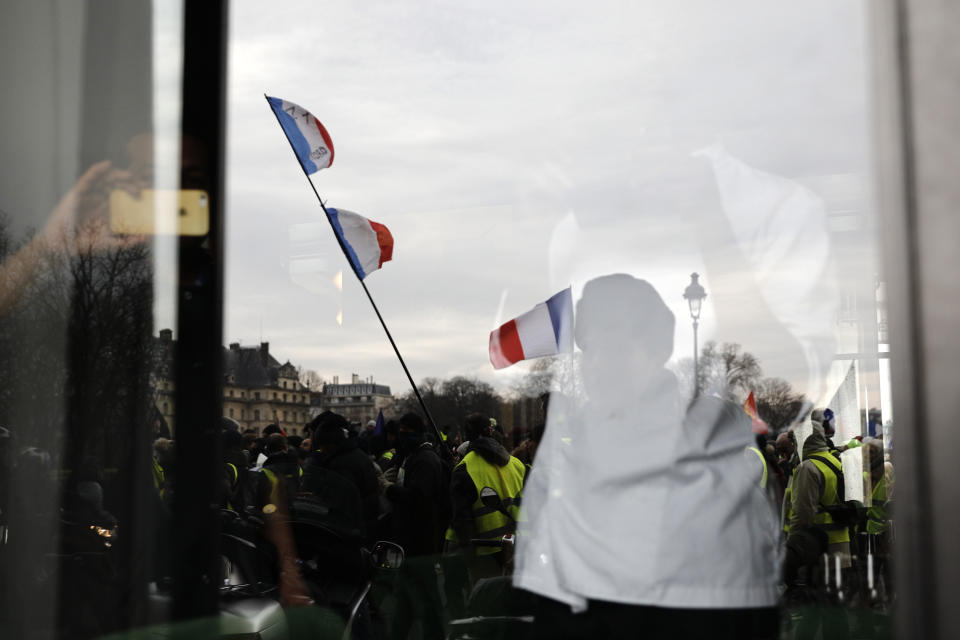 Yellow vest demonstrators are reflected in a window during a march in Paris, Saturday, Jan.19, 2019. Yellow vest protesters are planning rallies in several French cities despite a national debate launched this week by President Emmanuel Macron aimed at assuaging their anger. (AP Photo/Kamil Zihnioglu)