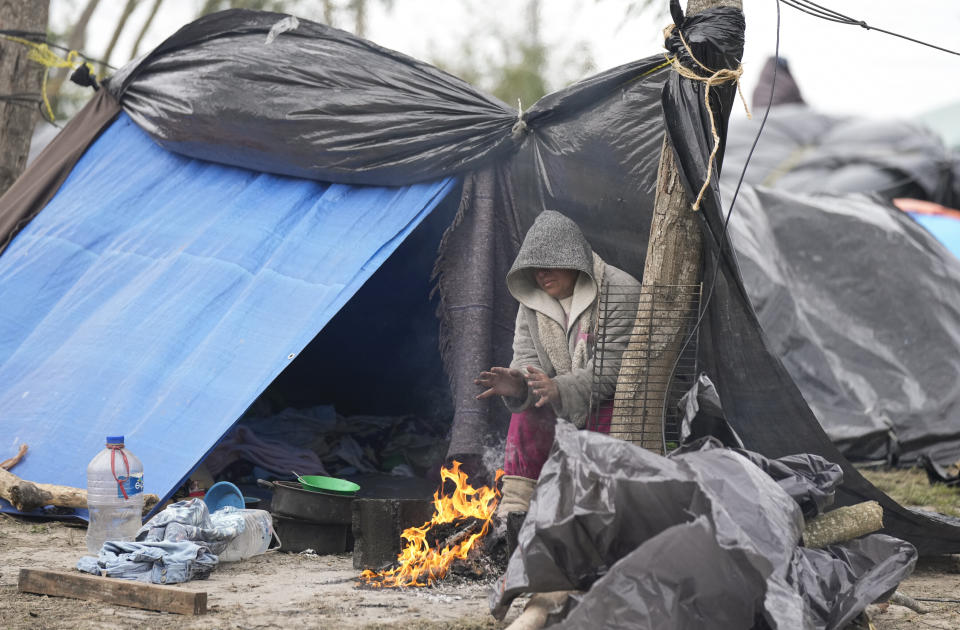 Una migrante venezolana se calienta las manos frente a una fogata junto a su tienda improvisada, negándose a ser reubicada en un albergue para refugiados, el viernes 23 de diciembre de 2022, en Matamoros, México. (AP Foto/Fernando Llano)