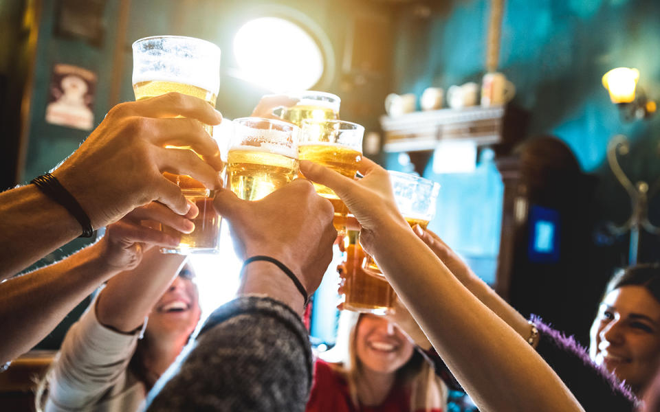 Photo shows a group of people toasting with full beer glasses.