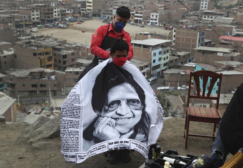 El peluquero Josué Yacahuanca amarra a un cliente una cubierta que lleva la imagen del cantante Héctor Lavoe en una colina del barrio San Juan de Lurigancho en Lima, Perú, el viernes 19 de junio de 2020. (AP Foto/Martin Mejia)