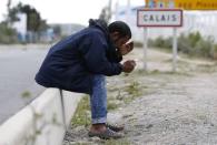 A migrant looks at his mobile phone as he sits near a road sign on the main access route to the Ferry harbour Terminal in Calais, northern France, July 30, 2015. REUTERS/Pascal Rossignol