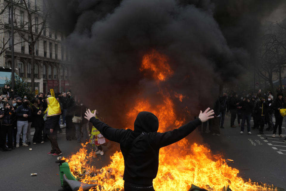 FILE - A man gestures at a burning garbage cans during a demonstration Tuesday, March 28, 2023 in Paris. With President Emmanuel Macron thousands of miles away in China, French protesters and unions returning to the streets continue to reveal cracks in his domestic political authority. Hundreds of thousands are expected again for the 11th day of nationwide resistance to raising the retirement age from 62 to 64 Thursday, April 6 as the controversial law is being considered by the Constitutional Council. (AP Photo/Thibault Camus, File)