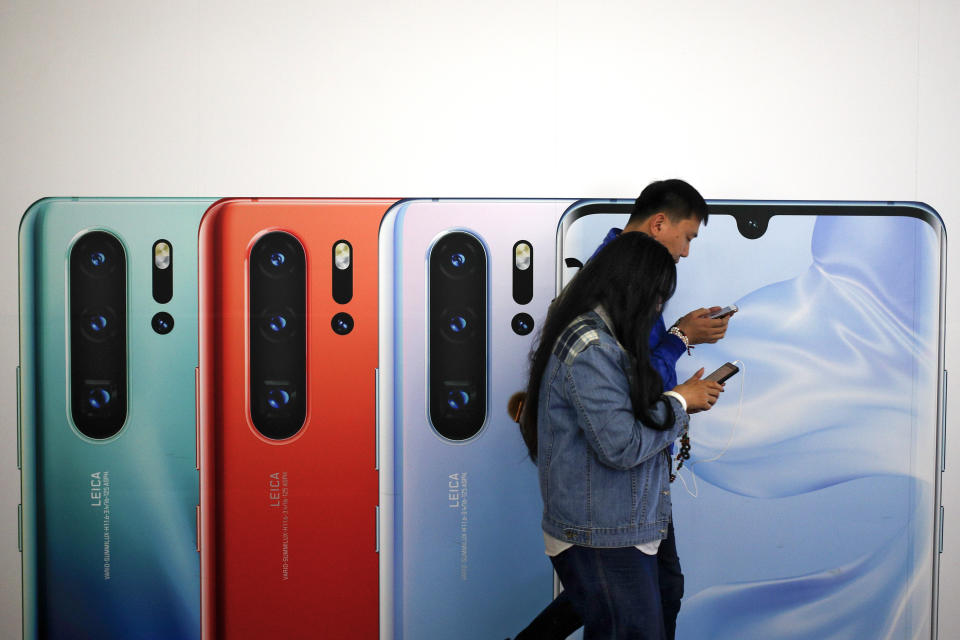 Una pareja china revisa sus smartphones mientras pasan frente a un anuncio sobre el nuevo smartphone Huawei P30 en una estación del metro en Beijing, el lunes 13 de mayo de 2019. (AP Foto/Andy Wong)