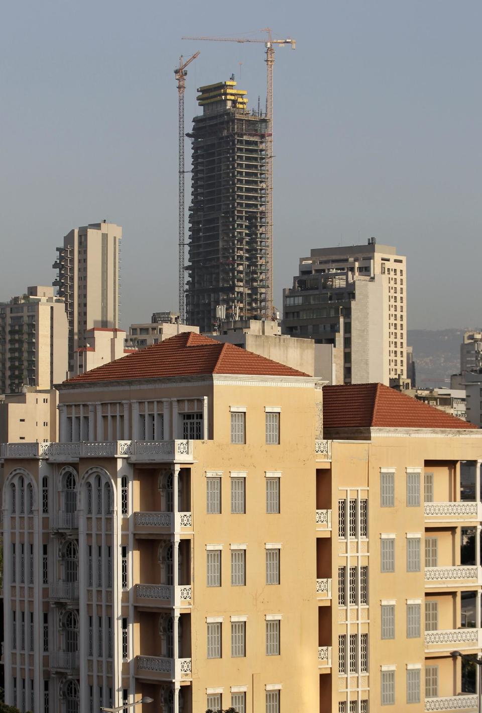 In this April 8, 2014 photo, an old building with a traditional red brick roof, foreground, is overshadowed by the Beirut Sky tower under construction in Beirut, Lebanon. One by one, the old traditional houses of Beirut are vanishing as luxury towers sprout up on every corner, altering the city's skyline almost beyond recognition. While Lebanon's real estate sector has developed to become one of the country's success stories, many say it is coming at the expense of Lebanon's identity and heritage. (AP Photo/Hussein Malla)