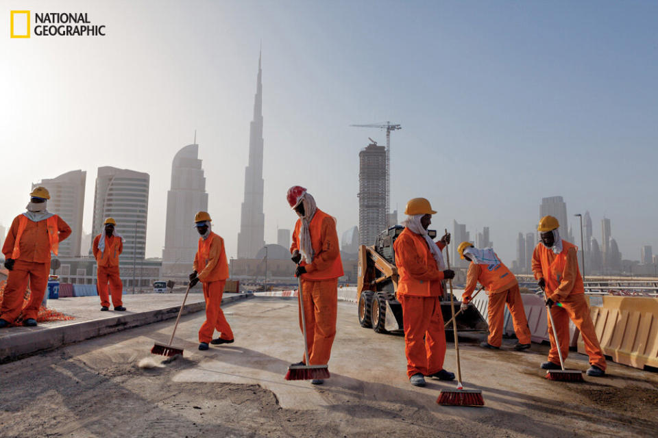 The world’s tallest building, the Burj Khalifa, looms like a distant bayonet over workers cleaning up a construction site in Dubai. The sweepers are mostly from Pakistan and India.