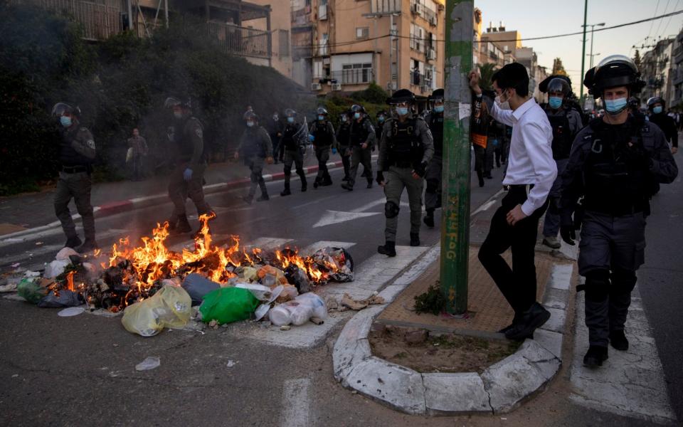 Israeli police officers march by burning garbage during clashes with ultra-Orthodox Jews in Bnei Brak, Israel - Oded Balilty/AP Photo