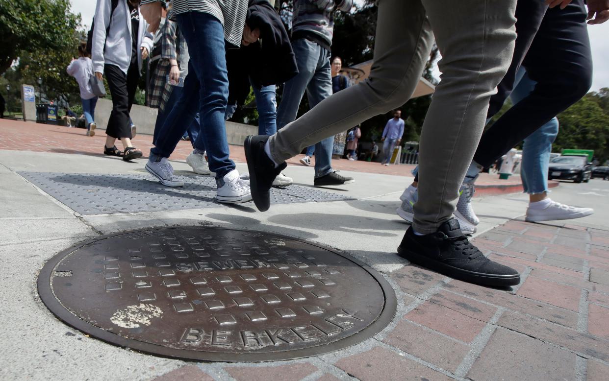 Pedestrians walk past a manhole cover for a sewer in Berkeley, Calif., Thursday, July 18, 2019.