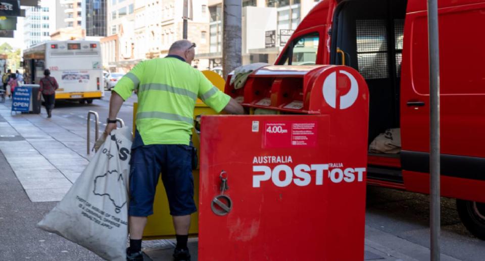 Australia Post contractor loading mail into a bag from a mailbox, Australia Post van in background