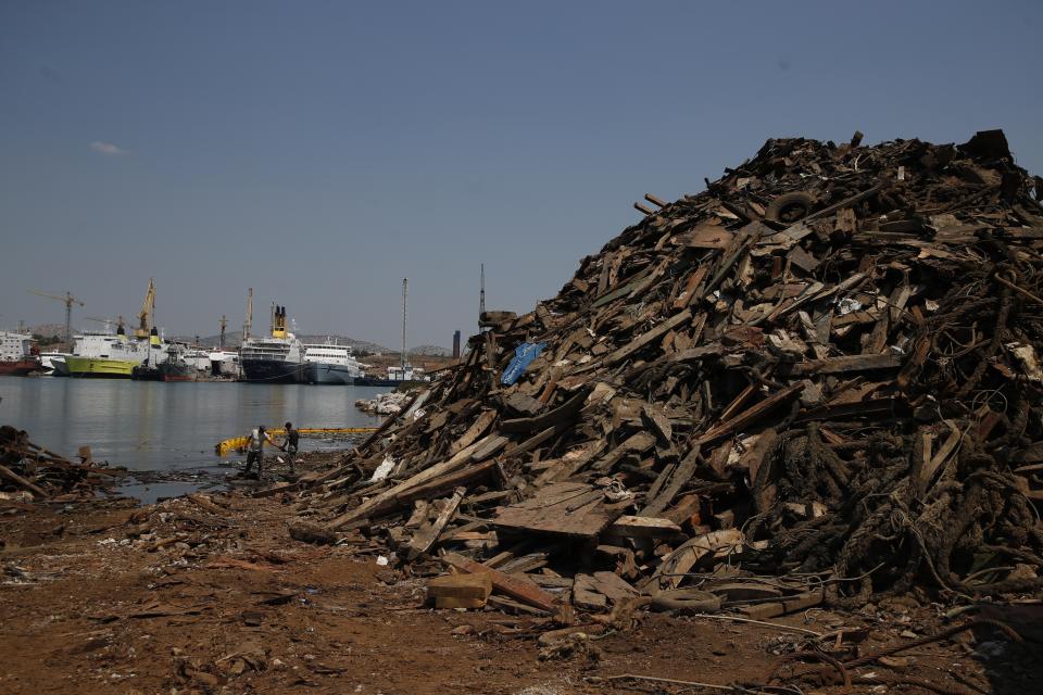 Workers clean the sea next to a pile of debris from destroyed wooden yachts on Salamina island, west of Athens, on Wednesday, July 1, 2020. Greece this year is commemorating one of the greatest naval battles in ancient history at Salamis, where the invading Persian navy suffered a heavy defeat 2,500 years ago. But before the celebrations can start in earnest, authorities and private donors are leaning into a massive decluttering operation. They are clearing the coastline of dozens of sunken and partially sunken cargo ships, sailboats and other abandoned vessels. (AP Photo/Thanassis Stavrakis)