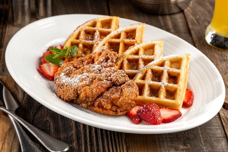 A plate of chicken and waffles garnished with strawberries