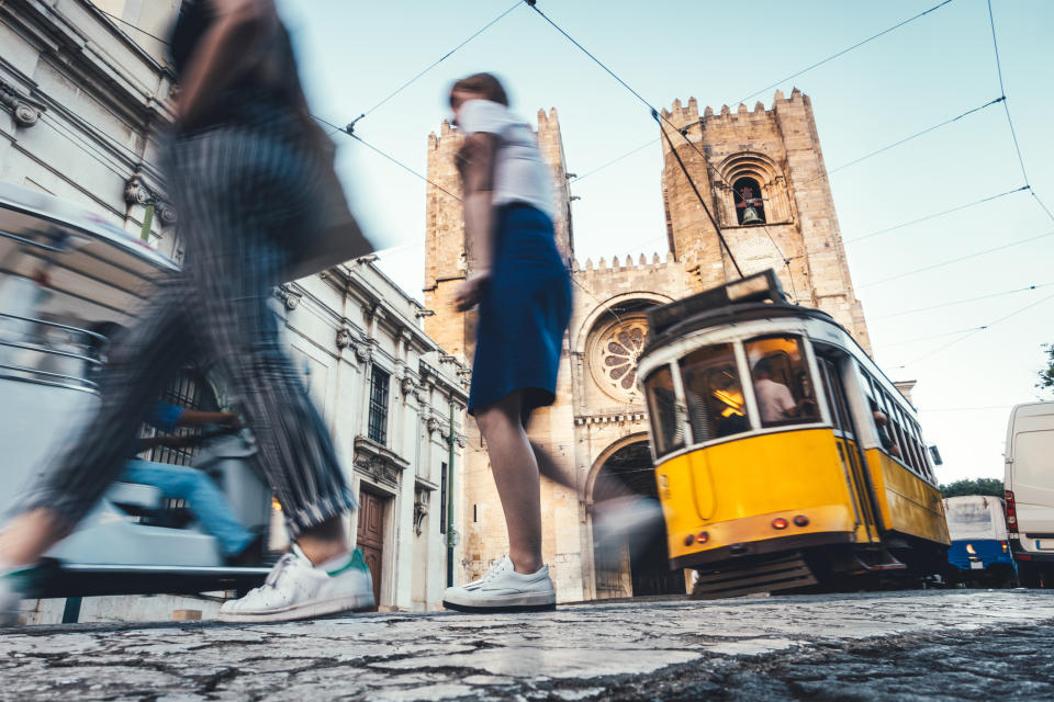 People in motion in a city with a tram and historical building in the background