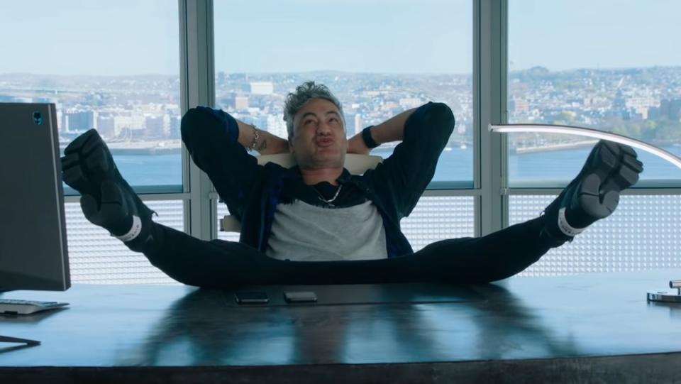 A man sits in a chair with his legs on the table and his arms behind his head in a room high in a skyscraper