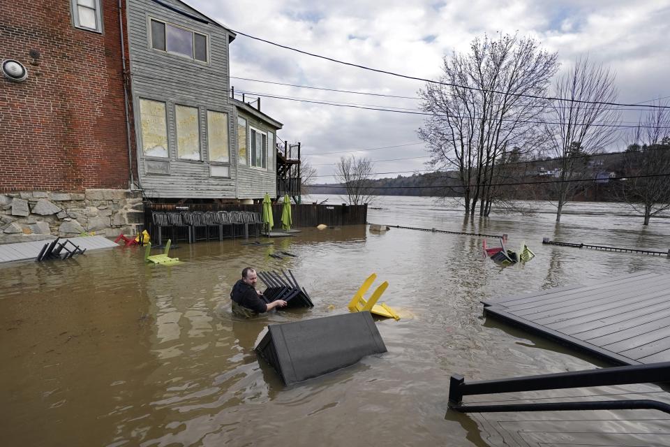 Nathan Sennett wades to retrieve furniture in hip-deep water on the patio of the Quarry Tap Room, Tuesday, Dec. 19, 2023, in Hallowell, Maine. Waters continue to rise in the Kennebec River following Monday's severe storm. (AP Photo/Robert F. Bukaty)
