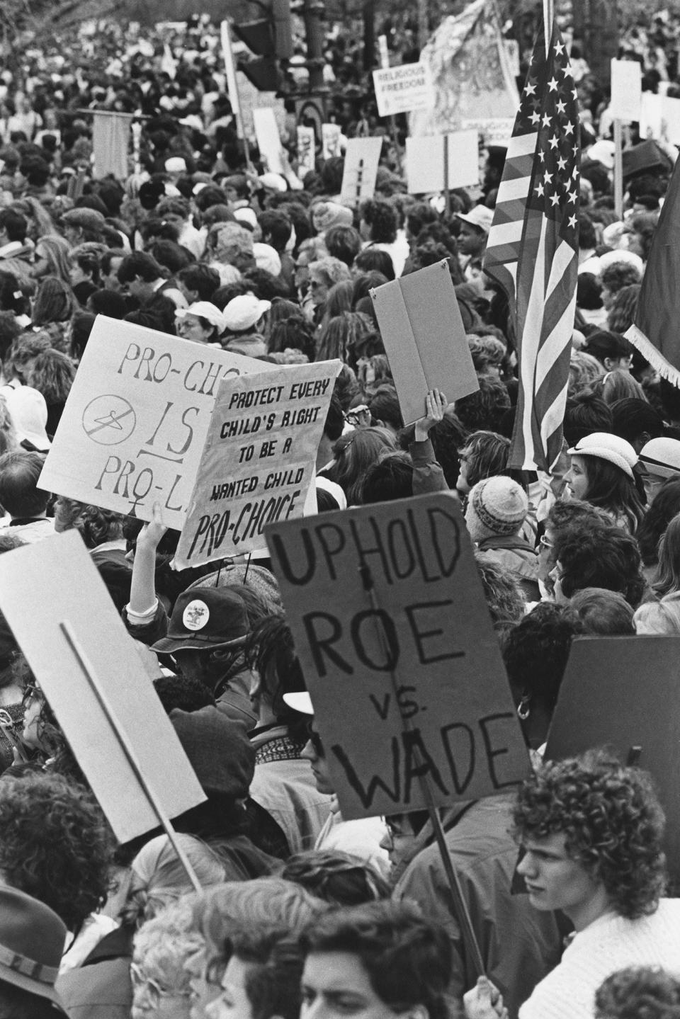 Demonstrators in a large crowd hold signs reading "uphold Roe v Wade" and "protect every child's right to be a wanted child" and "pro-choice is pro-life"