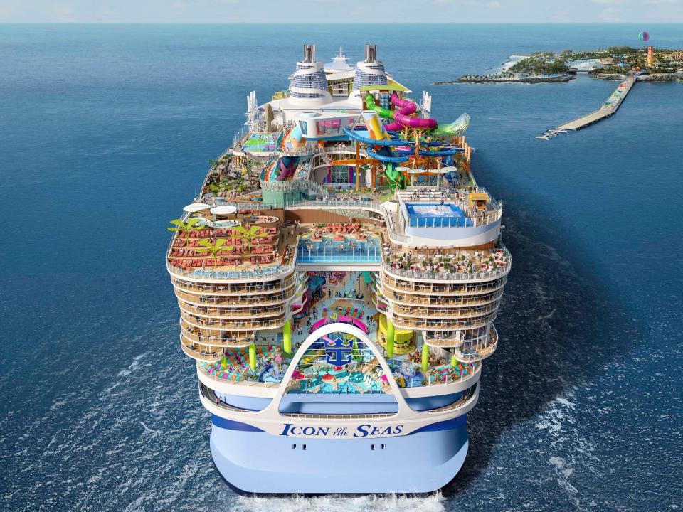 The back of the Icon of the Seas, which has multiple decks, water slides, and swimming pools,sailing alongside an island.