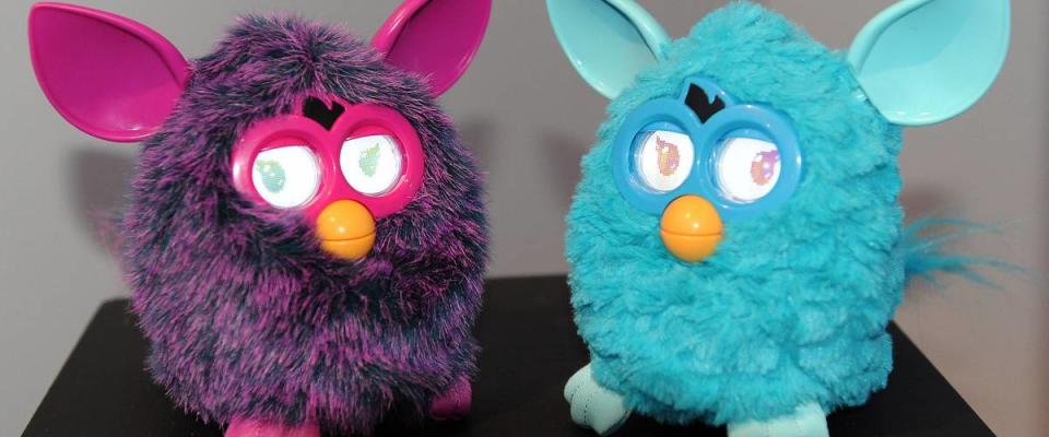 Two Furby dolls on a table, purple and blue